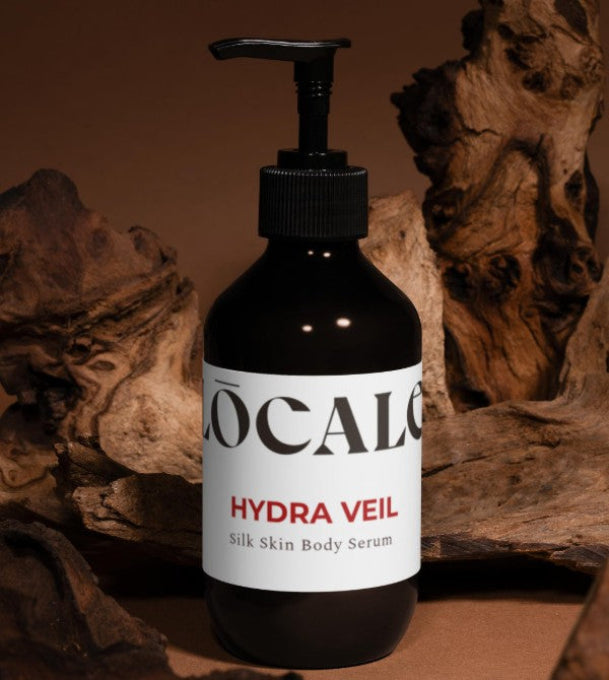 Black bottle of 'LOCALE' Hydra Veil Silk Skin Body Serum with a pump on a wooden background
